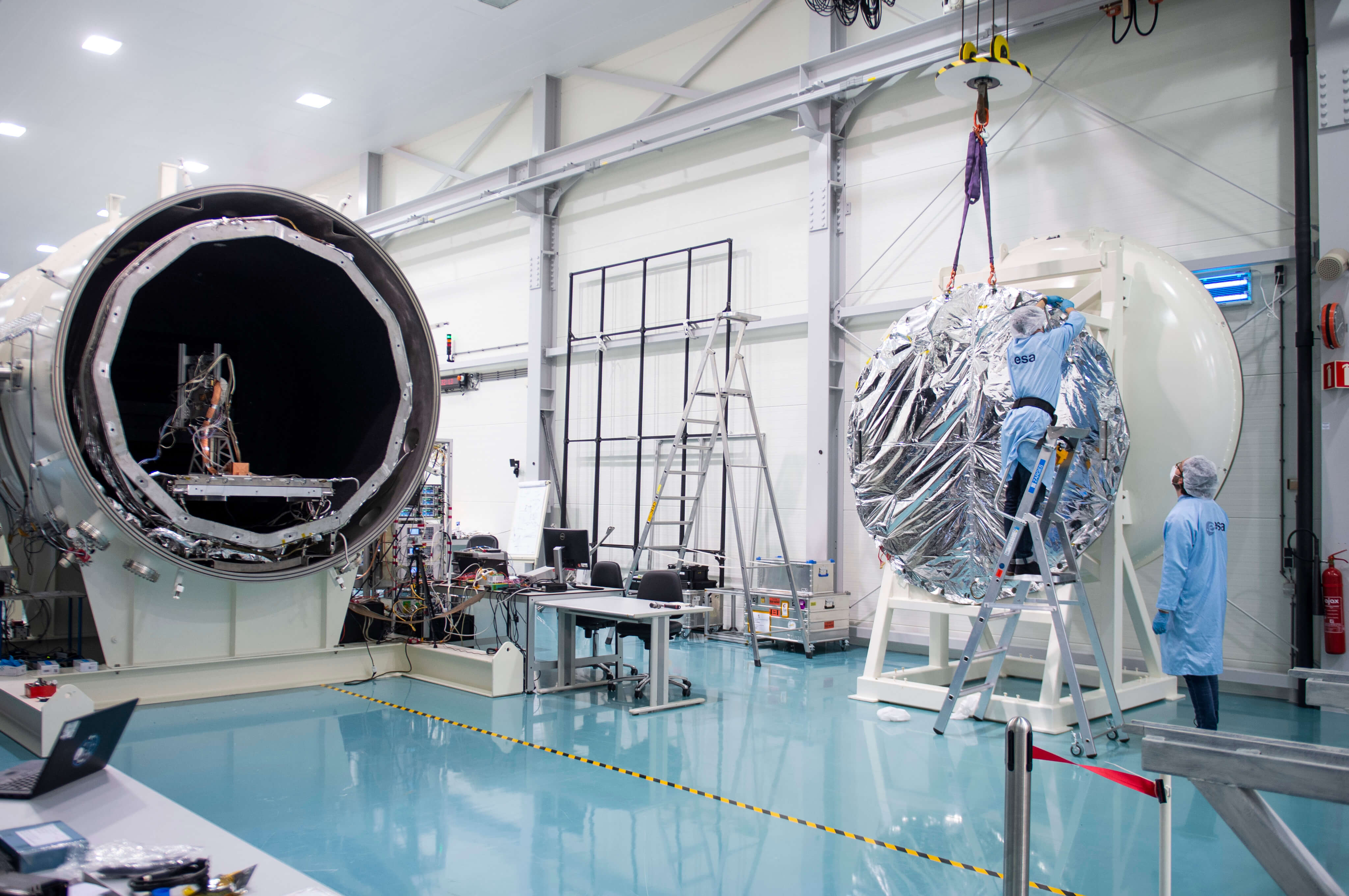 Preparations for testing in the LORENTZ test chamber. A large shiny foil disc is moved into position by a crane. Credits: ESA - G.Porter